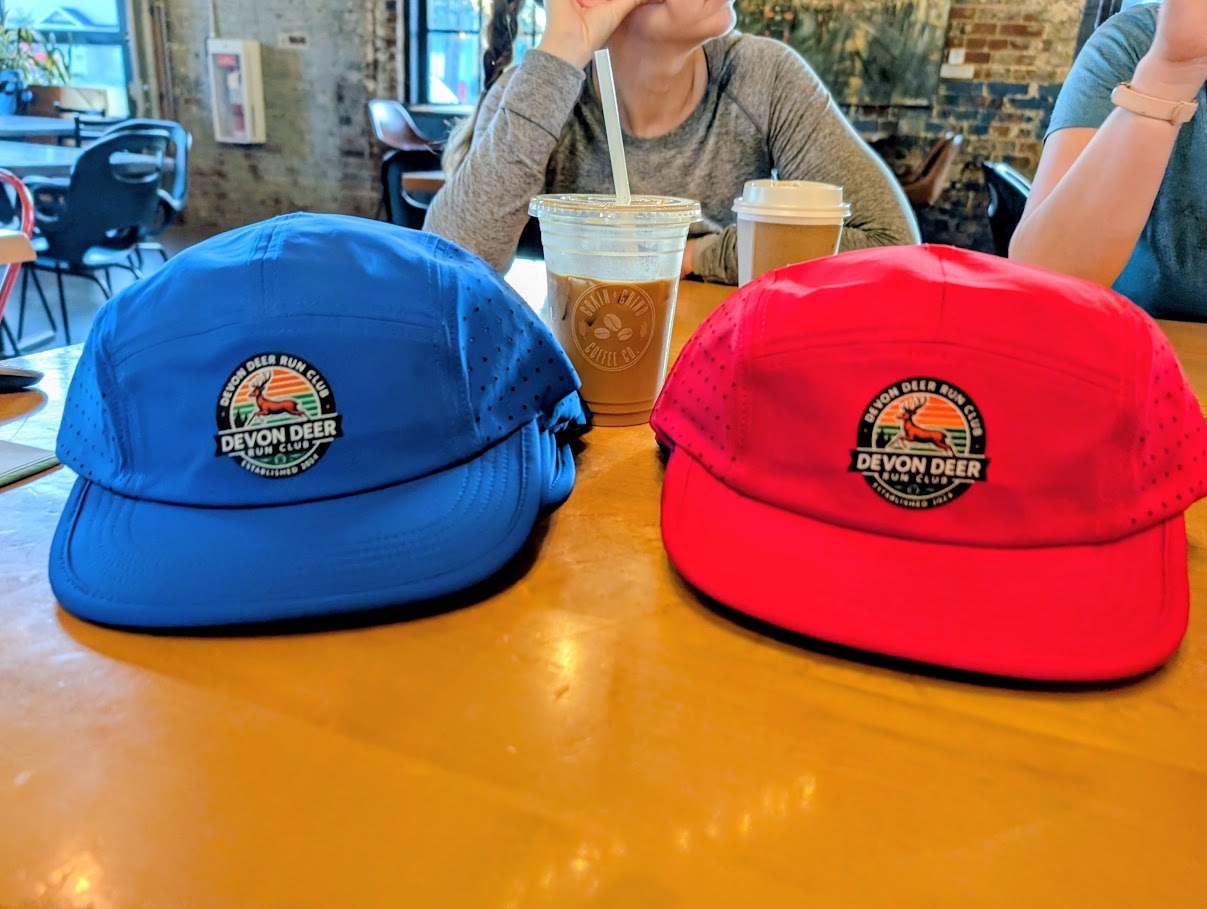 Une casquette Devon Deer bleue et une rouge sont posées sur une table avec des cafés de Grain & Grind.