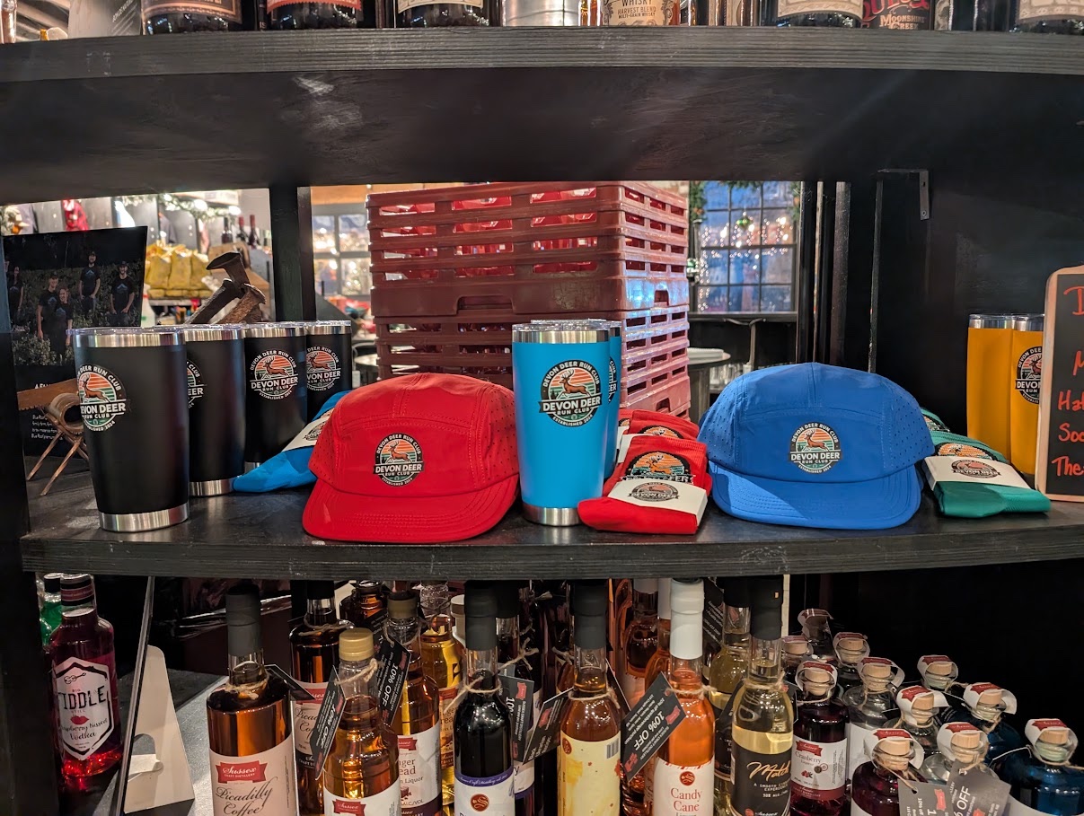 Des casquettes Devon Deer bleues et rouges, des chaussettes emballées et des gobelets isothermes sont disposés sur une étagère chez Picaroons Roundhouse.