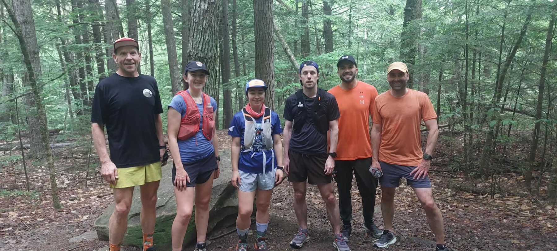 Six adult Devon Deer trail runners standing together among the trees in Odell Park.