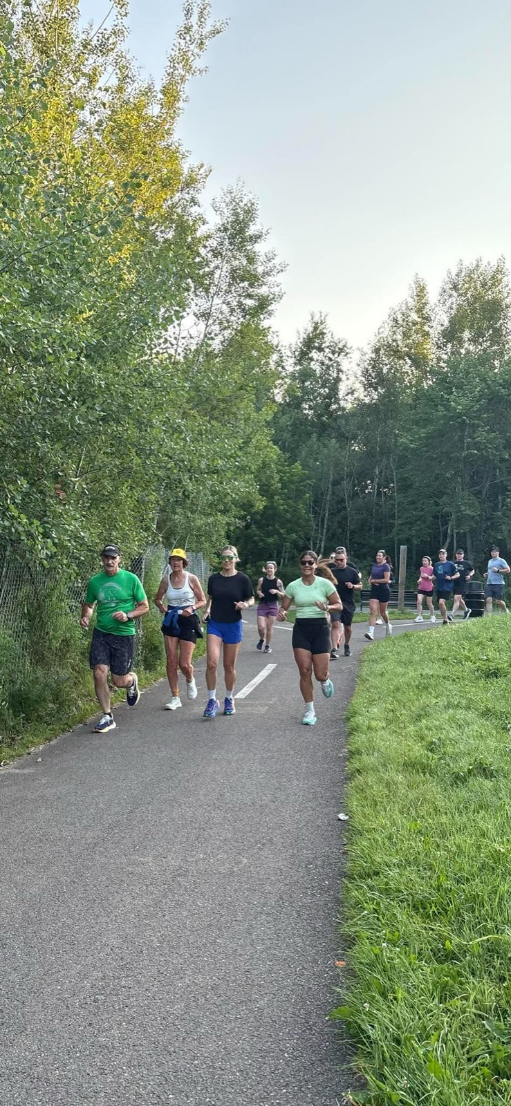A mixed-pace group of Devon Deer runners moving together along a green Fredericton riverside path.