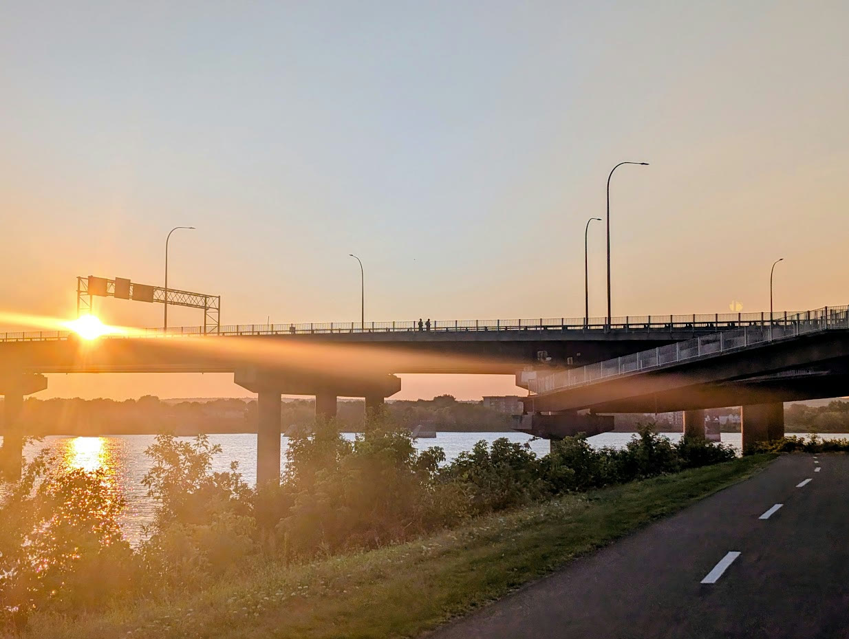 Two Devon Deer runners silhouetted at sunrise on the pedestrian path of Fredericton’s Westmorland Street Bridge above the Wolastoq.